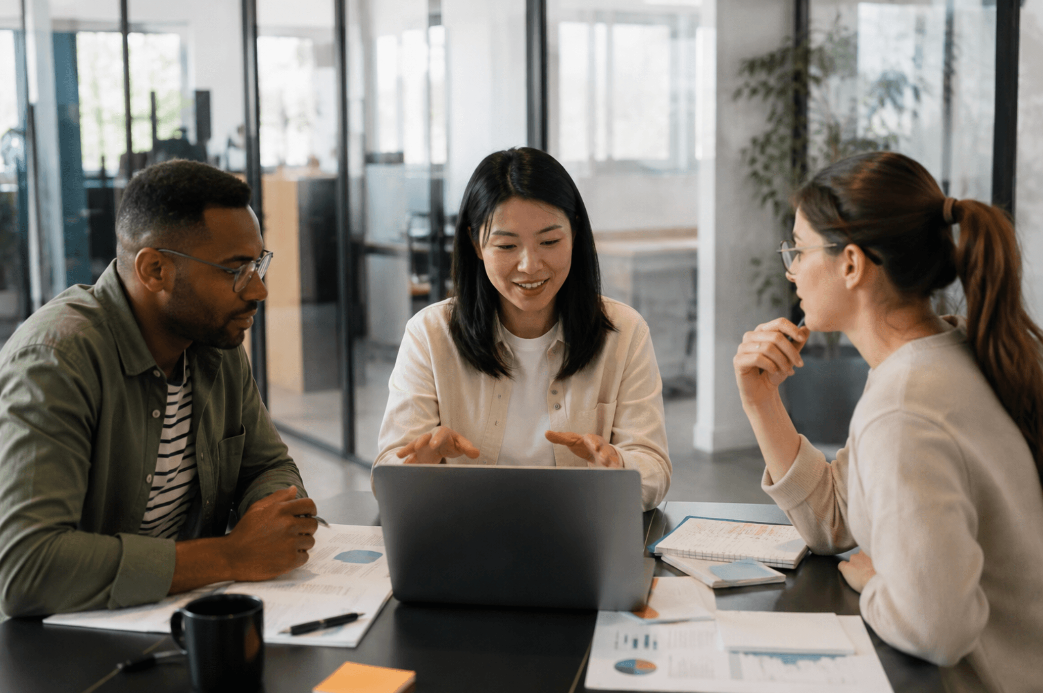 Employees collaborating around a laptop during a workplace training and team meeting in a modern office.